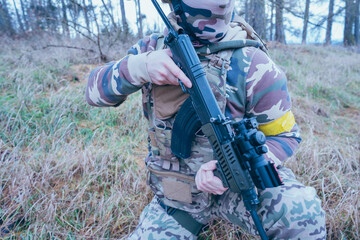 Fototapeta premium Ukrainian soldier on the front line. With an assault rifle in camouflage. Yellow tape. 