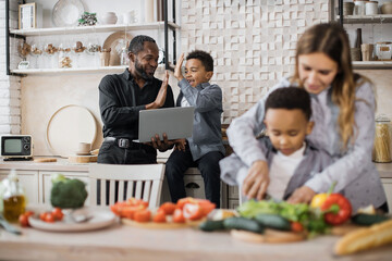 Focus on loving african father and small boy child finding recipe of holiday meal and giving high five. Happy mother teach little preschooler son chop vegetables preparing salad for lunch together.