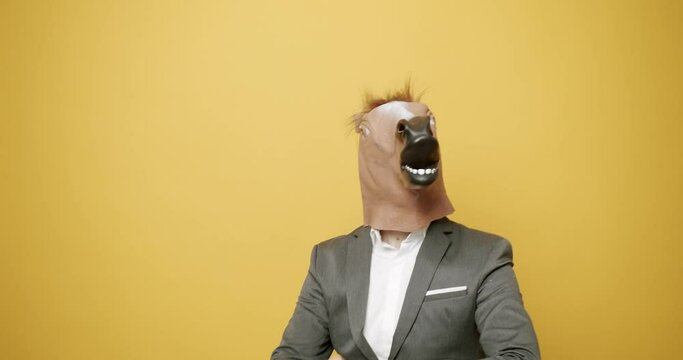  Static shot of weird man wearing suit and horse mask walking in dance and looking for confrontation while picking fight and looking away on yellow background