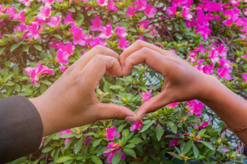 couple forming a heart with their hands in a garden