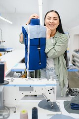 Positive young woman sewing with professional machine at workshop.