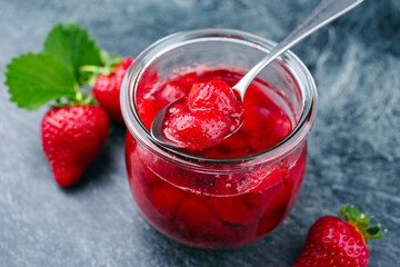 Reife rote Erdbeeren aus biologischem Anbau und Marmelade angeboten als close-up auf einem grauen Board