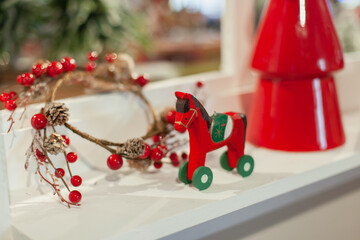 Classic red Christmas home decor with a horse toy, wreath and small xmas tree. Decorated window of the house for winter holiday season.