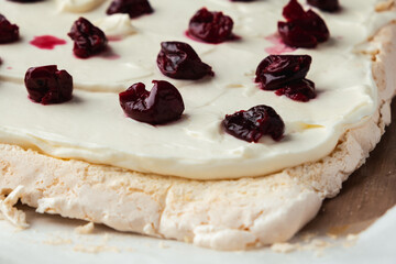 Cut of homemade meringue roll decorated with almond flakes and freeze-dried red cherries on the white marble background. Meringue roulade with whipped cream on a parchment paper