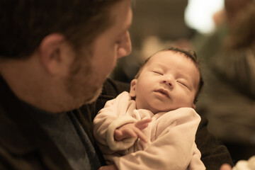 indoors lifestyle portrait of happy father holding his newborn baby girl only a few weeks old sitting on cafe taking care of the little daughter proud and cheerful