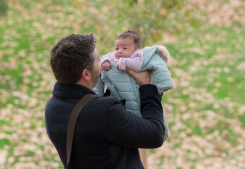 outdoors lifestyle portrait of happy father holding his newborn baby girl only a few weeks old sitting on city park bench taking care of the little daughter proud and cheerful