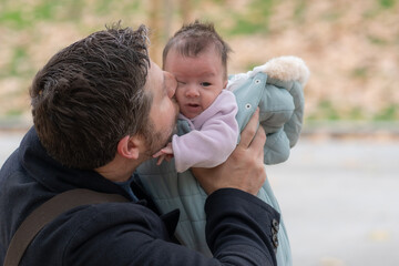 Fototapeta premium outdoors lifestyle portrait of happy father holding his newborn baby girl only a few weeks old sitting on city park bench taking care of the little daughter proud and cheerful