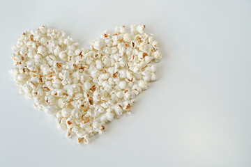 Popcorn heart, top view, on white, copy space. Close-up of heart lined with salted popcorn on the left side, high angle, room for text, light monochrome background, horizontal picture 
