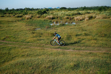 Obraz premium A young bearded cyclist is biking through a field