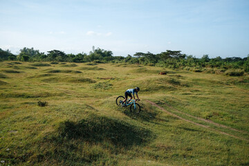 A young bearded cyclist is biking through a field