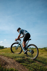 A young bearded cyclist is biking through a field