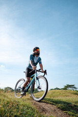 A young bearded cyclist is biking through a field