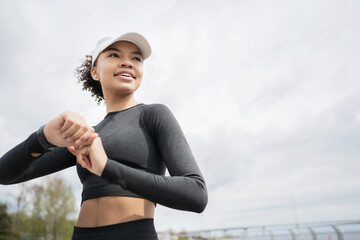 On the arm uses a fitness watch for sports. A young adult woman trains and runs in comfortable sportswear and a white cap. The coach is focused on routine work on the body.