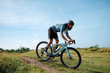 Fototapeta premium A young bearded cyclist is biking through a field