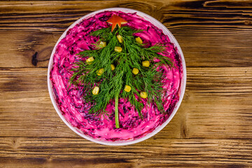Ceramic plate with russian traditional new year salad herring under fur coat (shuba) decorated with christmas tree made from dill on rustic wooden table. Top view
