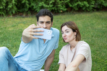 Young couple taking a photo on the picnic. Handsome man and his pretty wife taking a selfie sitting on the grass in the park