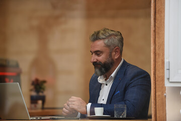Fototapeta premium Modern senior businessman sitting in cafe and using laptop and smartphone
