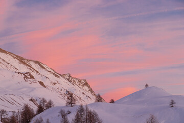 Luci rosse al crepuscolo. Sul lago gelato in mezzo alle  bianche distese di neve si specchiano i colori del cielo in alta montagna al confine tra Italia e Francia