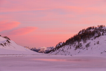 Luci rosse al crepuscolo. Sulle bianche distese di neve si specchiano i colori del cielo del crepuscolo in alta montagna al confine tra Italia e Francia