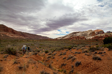 A group of hikers embarks on a trek through the Waterpocket Fold in Capitol Reef National Park, located in the desert region of southern Utah. The sky is full of clouds.