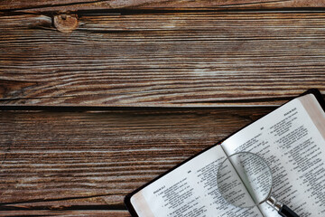 Holy bible book with magnifying glass on wooden table. Top view. Copy space. Searching, studying,...
