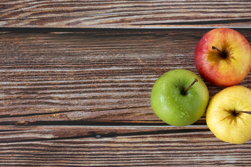 Three apples (red, green, and yellow) on wooden table. Top view. Copy space. Fresh organic autumn fruit in different colors.