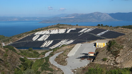 View of a sanitary landfill with sea and mountains in the background. Landfills emit methane which...