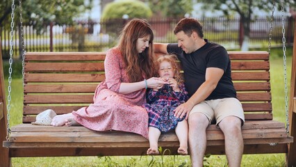 Portrait of a young family on a swing in the garden.