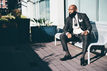 A black dandy man sits on a bench