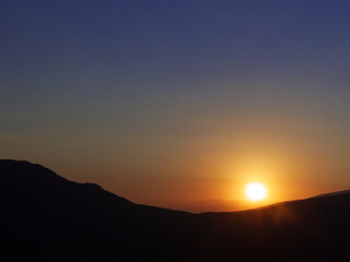 Sonnenuntergang an wolkenlosem himmel vor bergen als silouhette