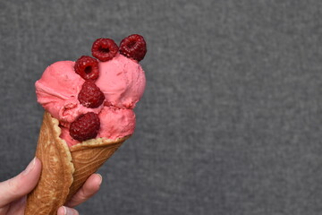 Raspberry ice cream in hand against grey background