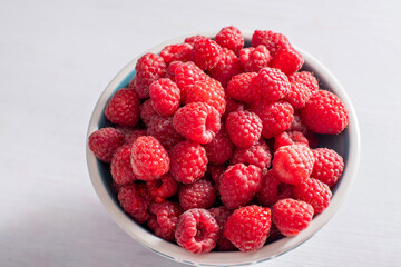 fresh raspberries in a blue bowl at the white table,summer harvest fresh berries