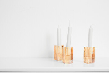 Holders with candles on shelf near white wall