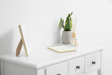 Blank photo frame, reed diffuser, houseplant and notebook on table near white wall