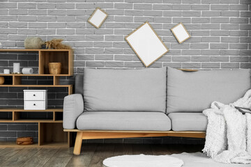 Sofa, shelf unit and blank photo frames on grey brick wall in living room