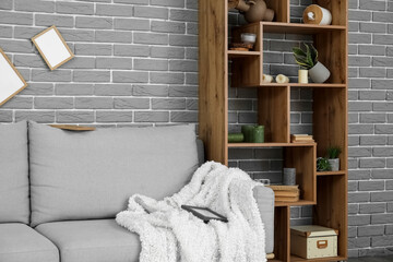 Sofa and shelf unit with overturned decor near grey brick wall in living room