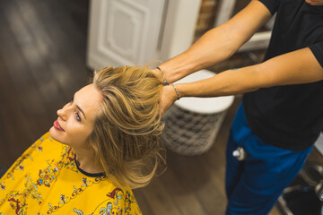 Hairstylist touching long blond hair of his young adult woman client. Top view. Copy space. Blurred background. High quality photo
