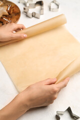 Female hands with baking paper and different cookie cutters on light background, closeup