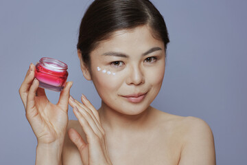 young woman with facial cream jar and facial cream on face