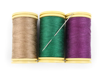 Colorful thread spools with needle on white background