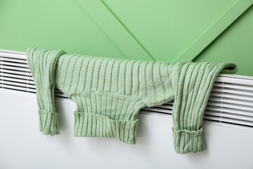 Warm sweater drying on electric radiator near green wall, closeup