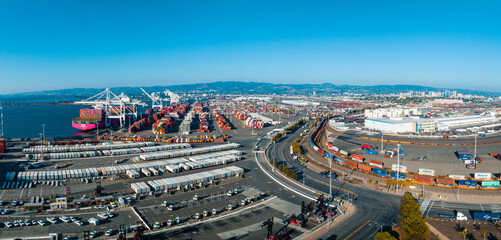 The Oakland Outer Harbor aerial view. Loaded trucks moving by Container cranes. View of busy Port of Oakland. Shipping terminal facility. - obrazy, fototapety, plakaty