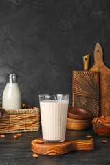 Wooden board with glass of almond milk on dark background