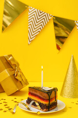 Birthday cake, party hat, gift, flags and confetti on yellow background