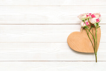 Beautiful rose flowers and heart figure on light wooden background