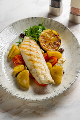sea bass fillet with grilled vegetables and lemon on marble table vertical