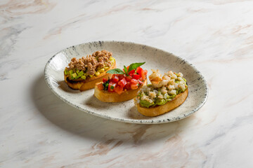 assorted bruschetts on plate, bruschetta with tuna and avocado, bruschetta with tomatoes and basil, bruschetta with shrimps on marble table