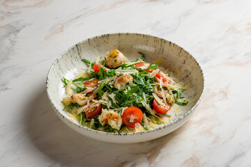 Arugula with shrimps, parmesan and tomatoes on marble table