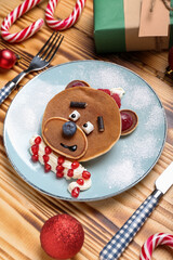 Plate with bear made of pancakes, fruits and Christmas decor on wooden table, closeup