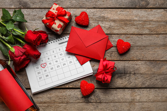 Calendar with marked date of Valentine's Day, envelopes, gifts, roses and wine bottle on dark wooden background